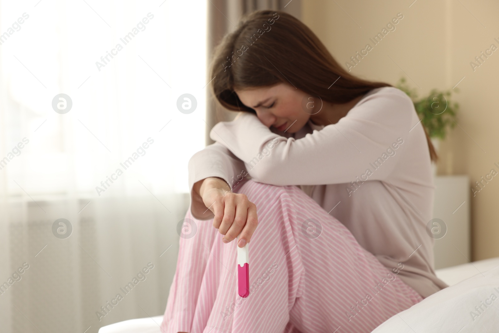 Photo of Upset woman with negative pregnancy test on bed at home, space for text