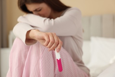 Photo of Upset woman with negative pregnancy test on bed at home, selective focus