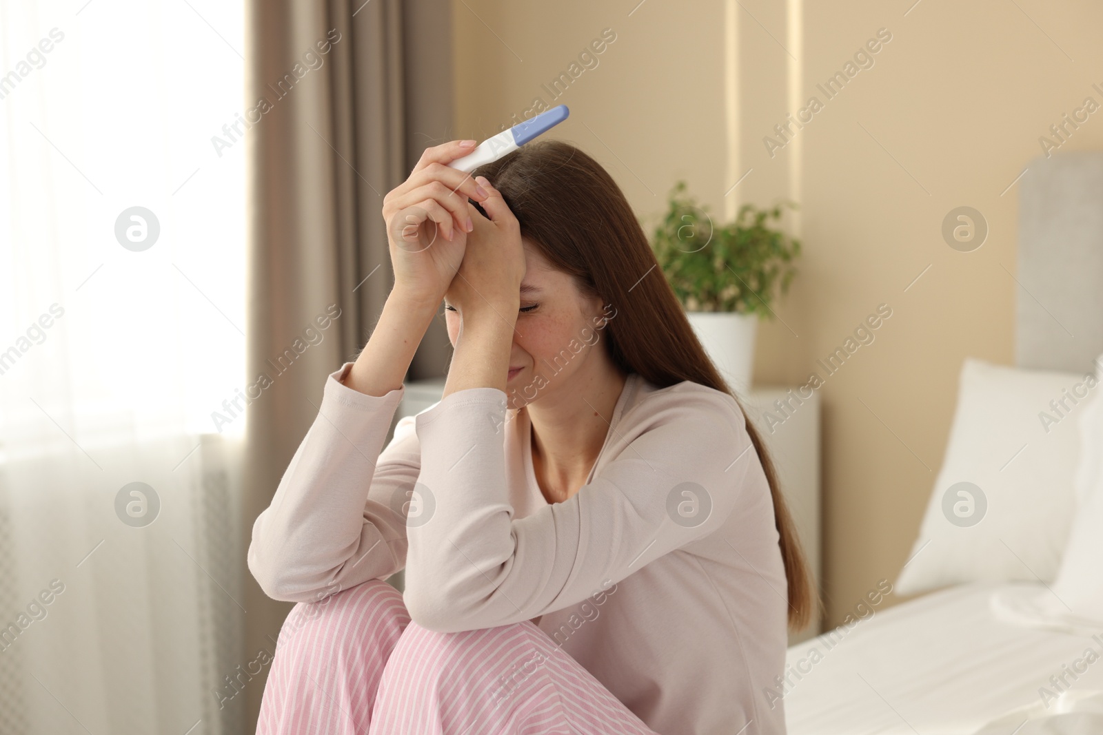 Photo of Upset woman with negative pregnancy test on bed at home