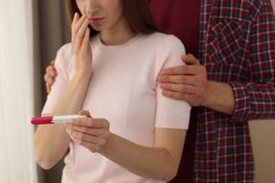 Woman with negative pregnancy test indoors, closeup. Man supporting his wife at home