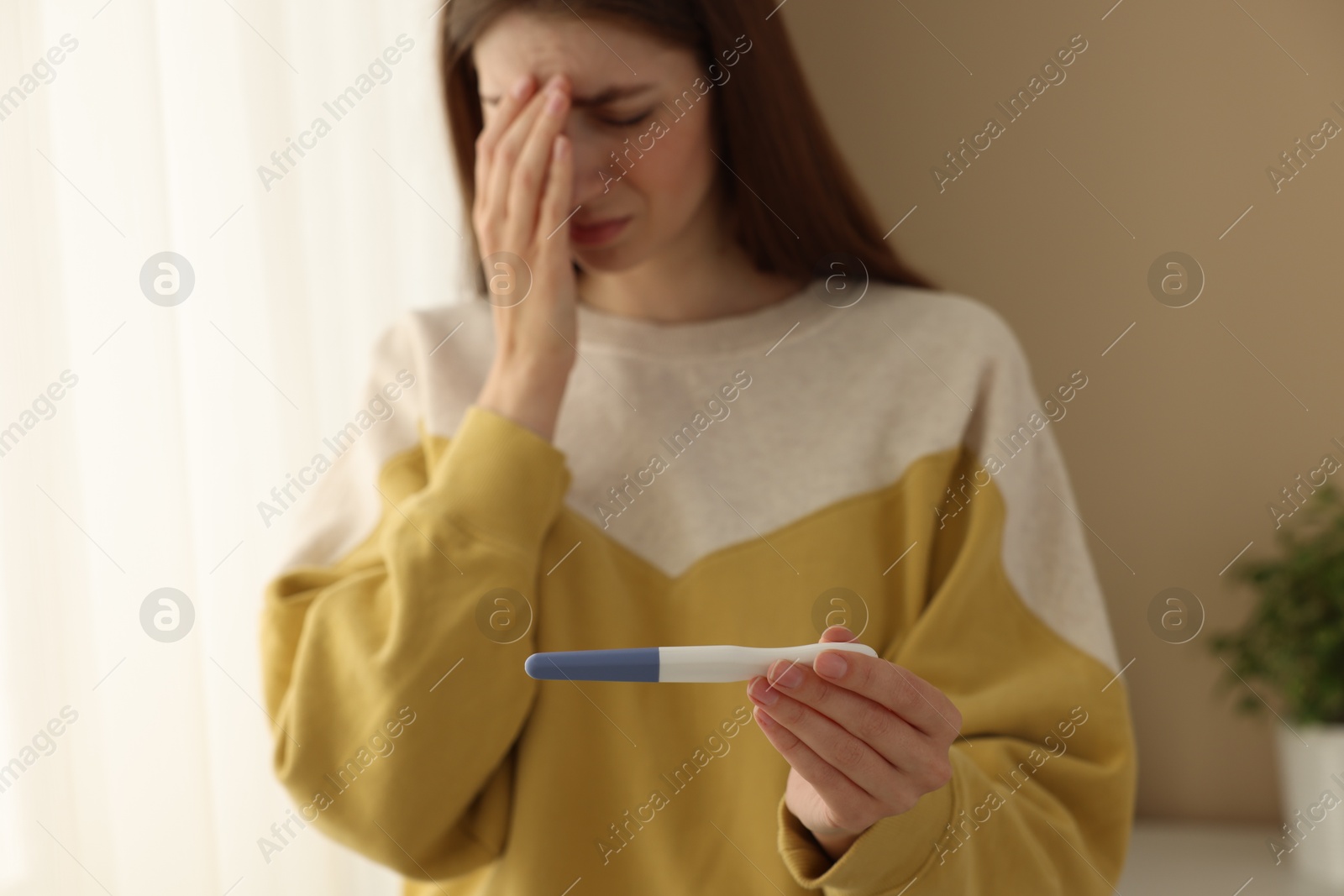 Photo of Upset woman with negative pregnancy test near window at home, selective focus