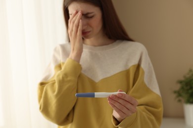 Upset woman with negative pregnancy test near window at home, selective focus