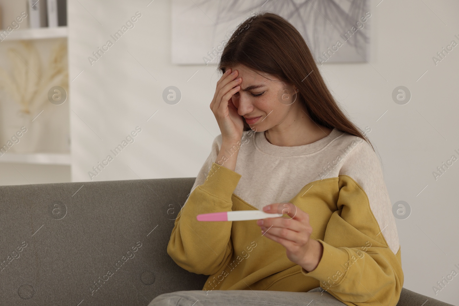 Photo of Upset woman with negative pregnancy test on sofa at home