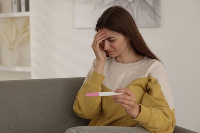 Photo of Upset woman with negative pregnancy test on sofa at home