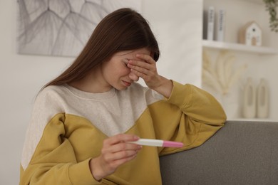 Photo of Upset woman with negative pregnancy test on sofa at home