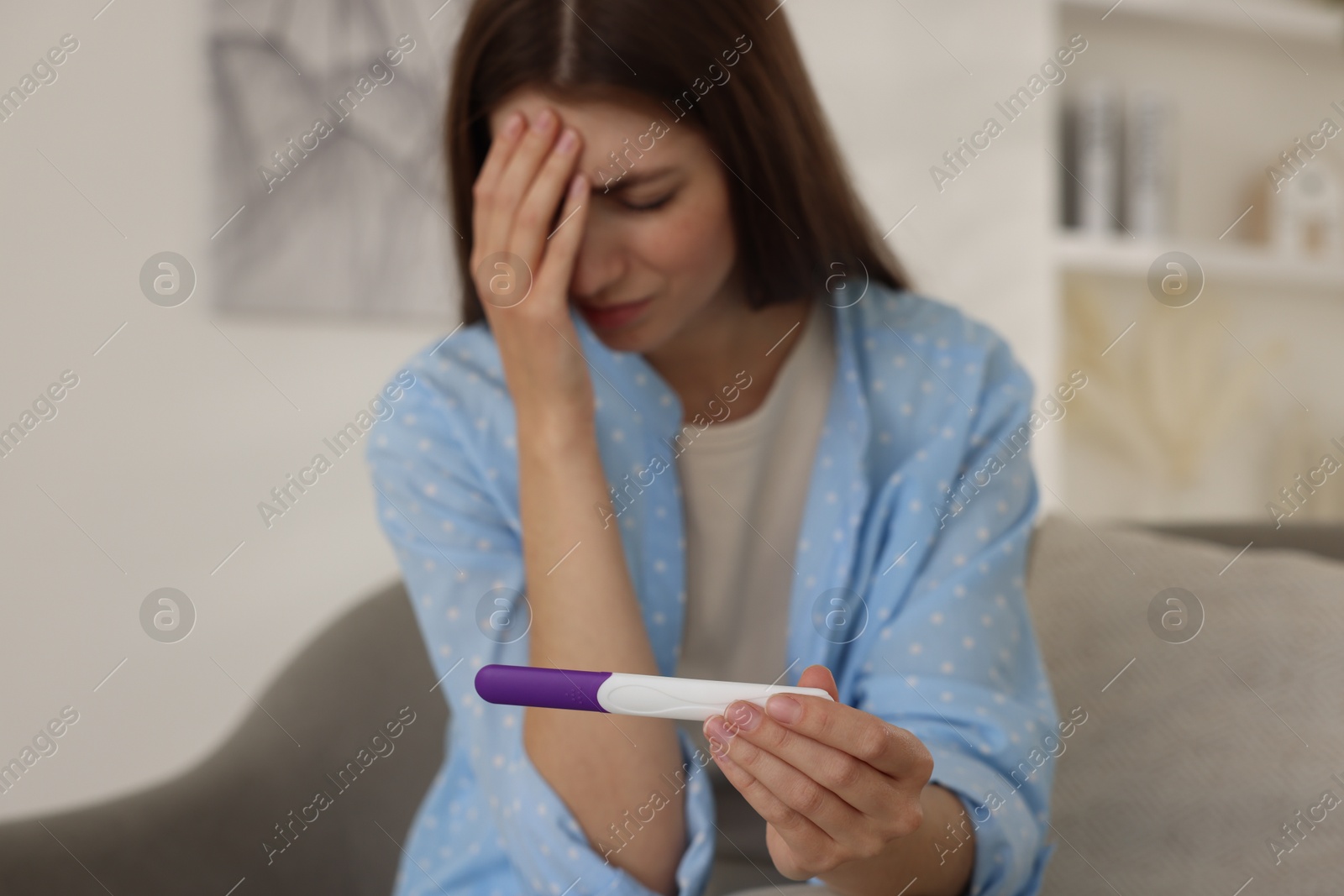 Photo of Upset woman with negative pregnancy test on sofa at home, selective focus