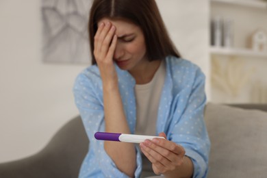 Photo of Upset woman with negative pregnancy test on sofa at home, selective focus