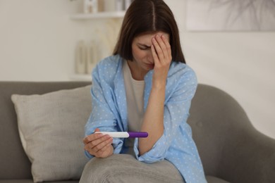 Photo of Upset woman with negative pregnancy test on sofa at home