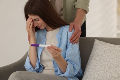 Upset woman with negative pregnancy test indoors. Man supporting his wife at home