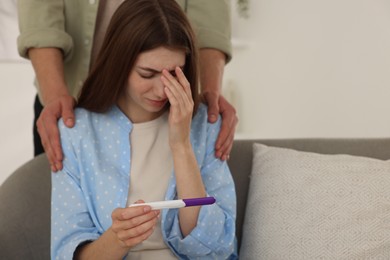 Upset woman with negative pregnancy test indoors. Man supporting his wife at home