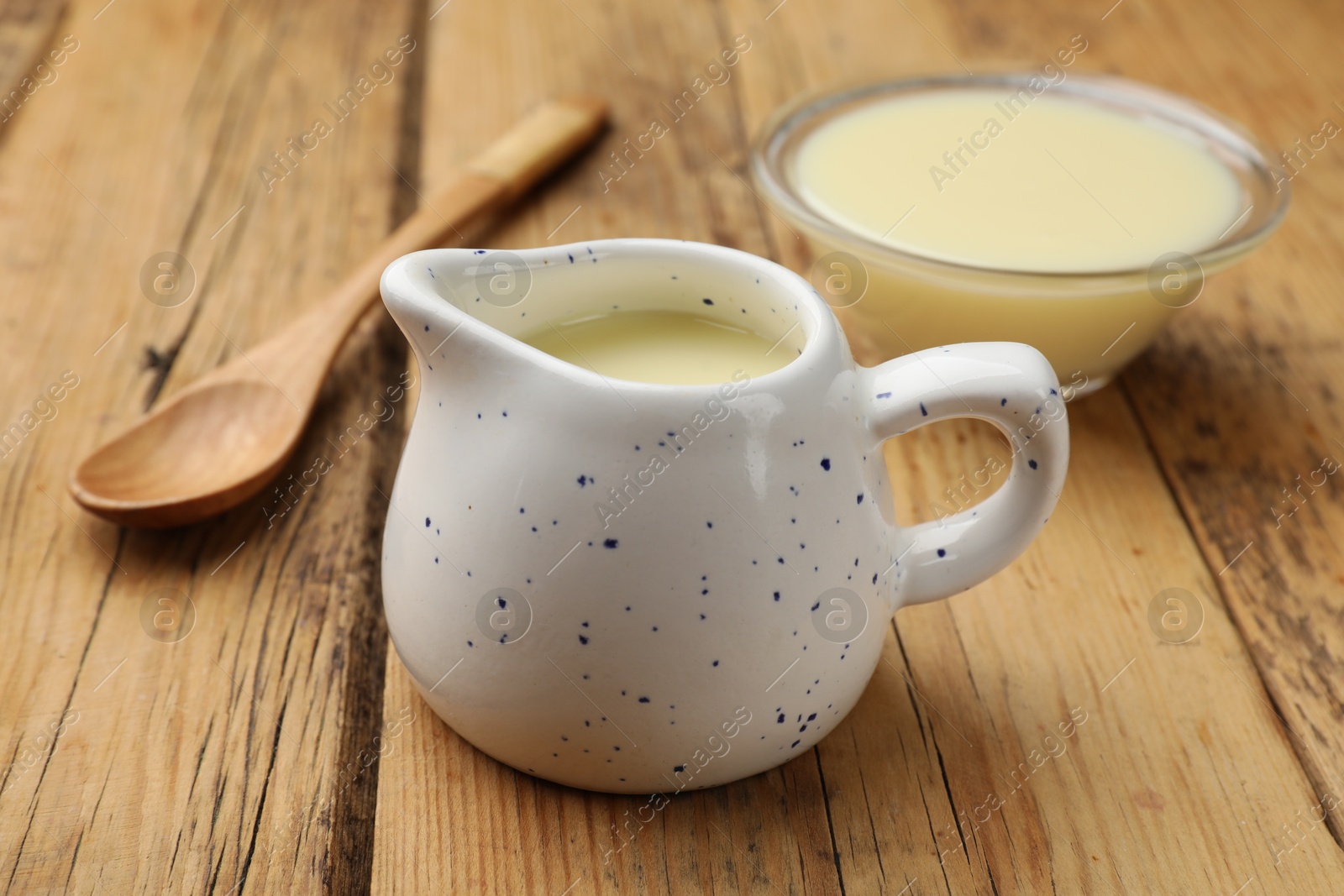 Photo of Condensed milk and spoon on wooden table, closeup