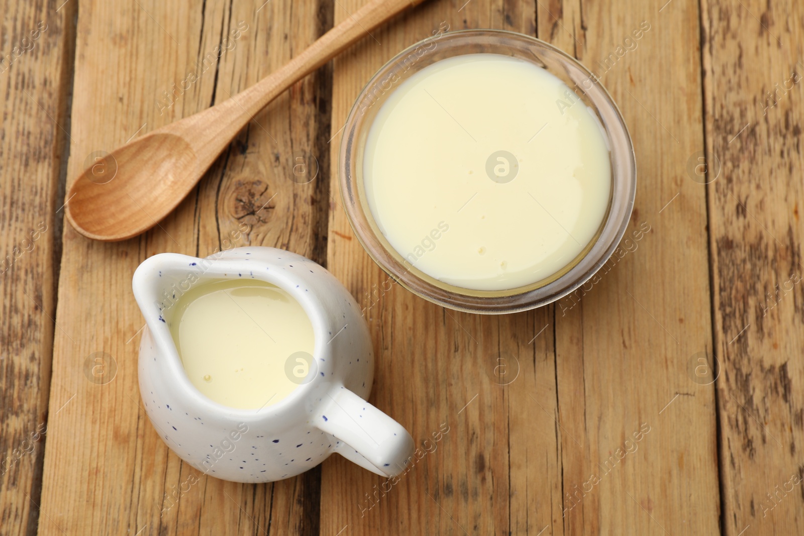 Photo of Condensed milk and spoon on wooden table, flat lay