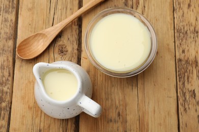 Photo of Condensed milk and spoon on wooden table, flat lay