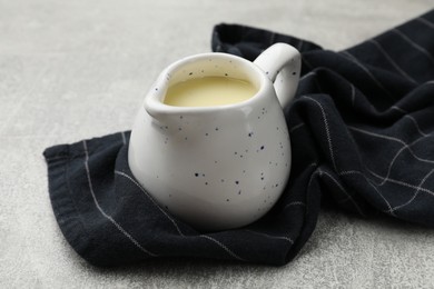 Photo of Condensed milk in jug on light grey table, closeup