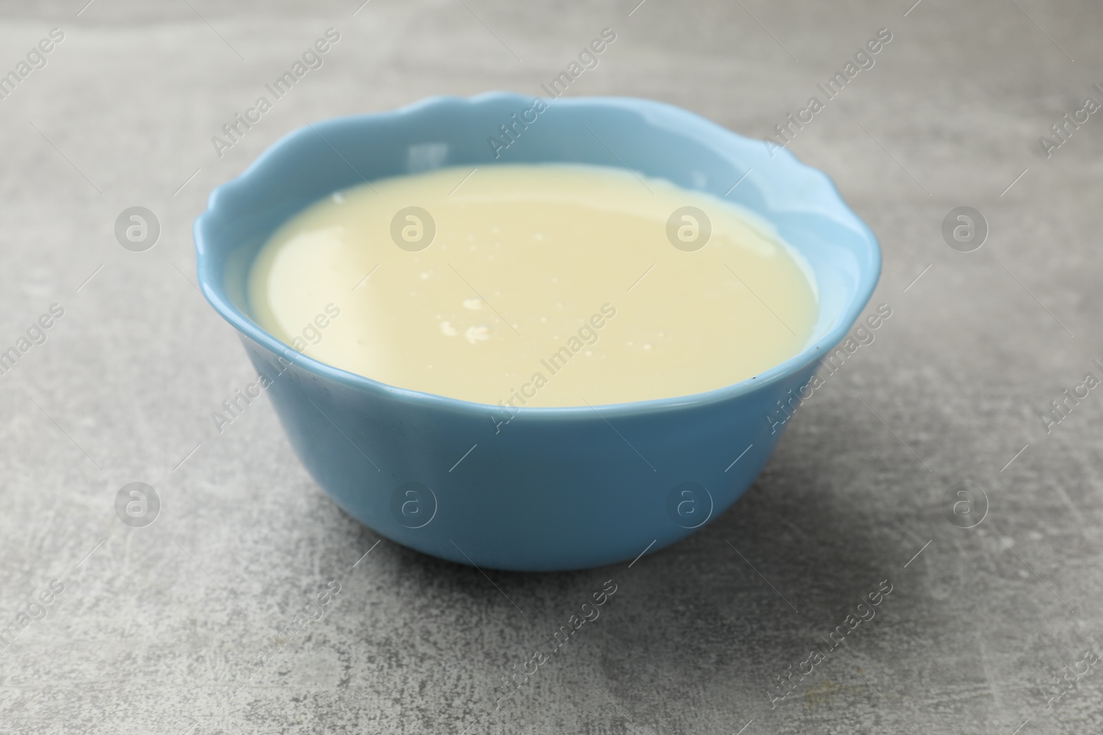 Photo of Condensed milk in bowl on light grey table, closeup