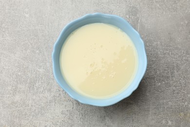 Photo of Condensed milk in bowl on light grey table, top view