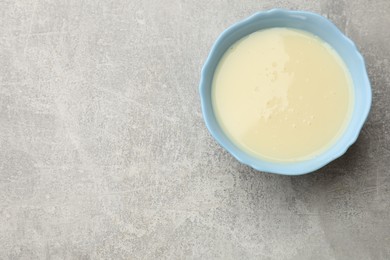 Photo of Condensed milk in bowl on light grey table, top view. Space for text