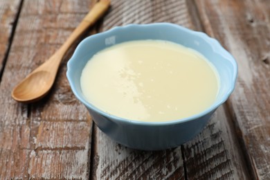 Photo of Condensed milk in bowl and spoon on wooden table, closeup