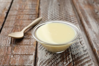 Photo of Condensed milk in bowl and spoon on wooden table, closeup