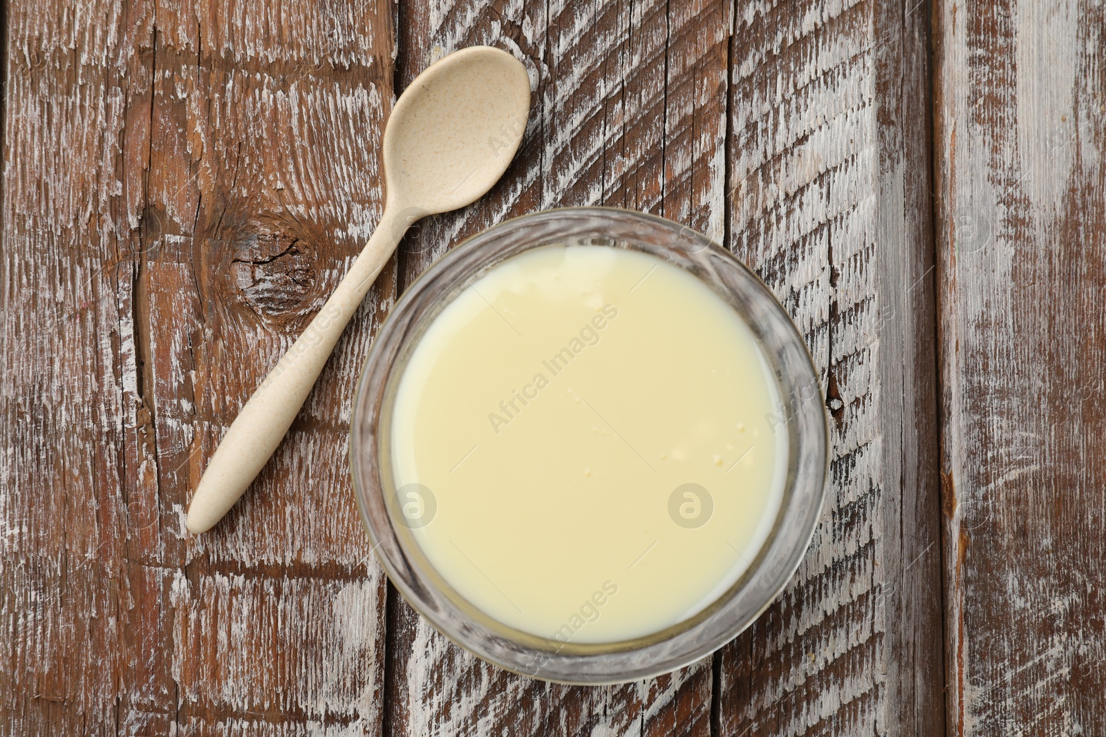 Photo of Condensed milk in bowl and spoon on wooden table, top view