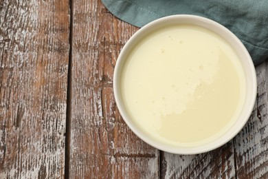 Photo of Condensed milk in bowl on wooden table, top view. Space for text