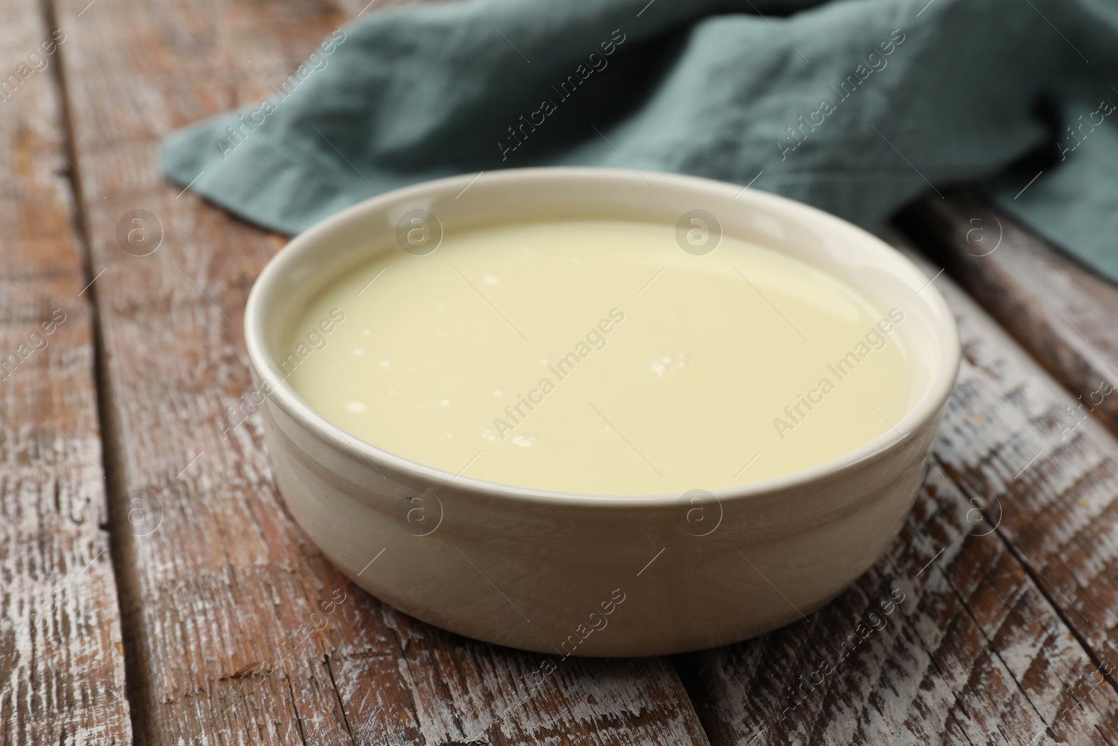 Photo of Condensed milk in bowl on wooden table, closeup