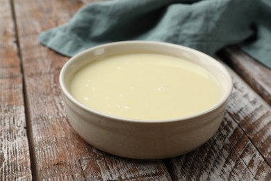 Photo of Condensed milk in bowl on wooden table, closeup