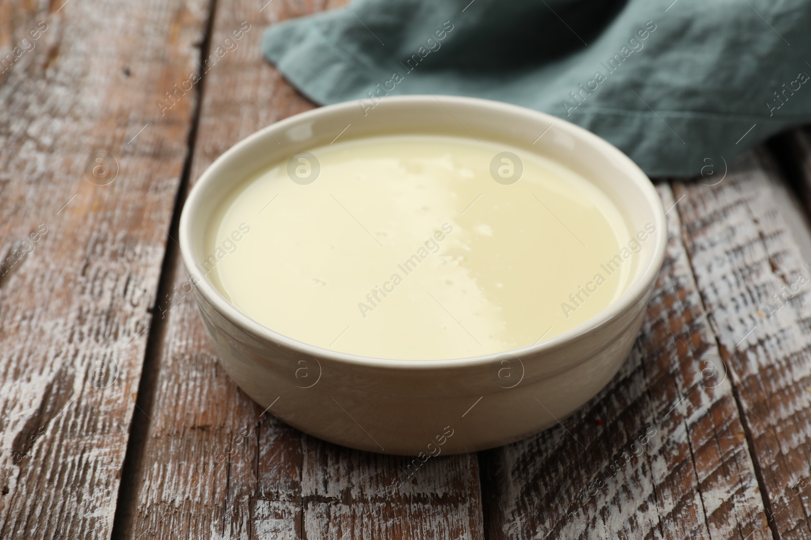 Photo of Condensed milk in bowl on wooden table, closeup