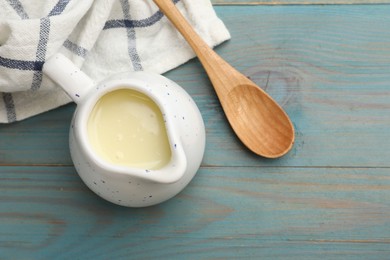 Photo of Condensed milk in jug and spoon on light blue wooden table, top view. Space for text