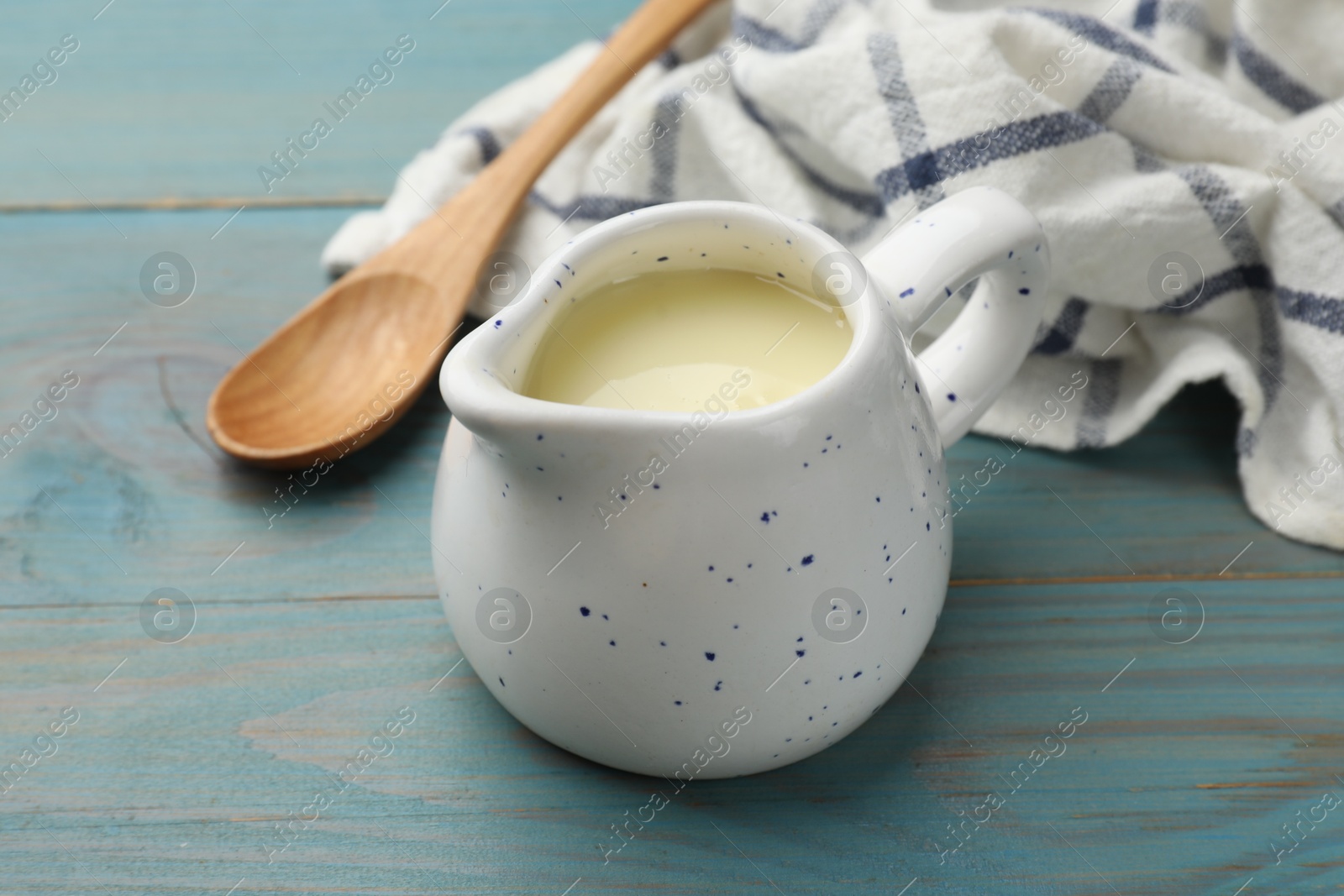 Photo of Condensed milk in jug and spoon on light blue wooden table, closeup