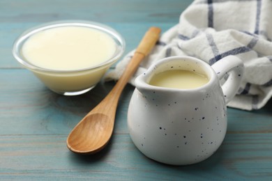 Photo of Condensed milk and spoon on light blue wooden table, closeup