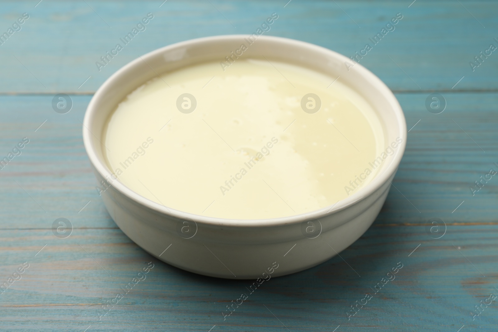 Photo of Condensed milk in bowl on light blue wooden table, closeup