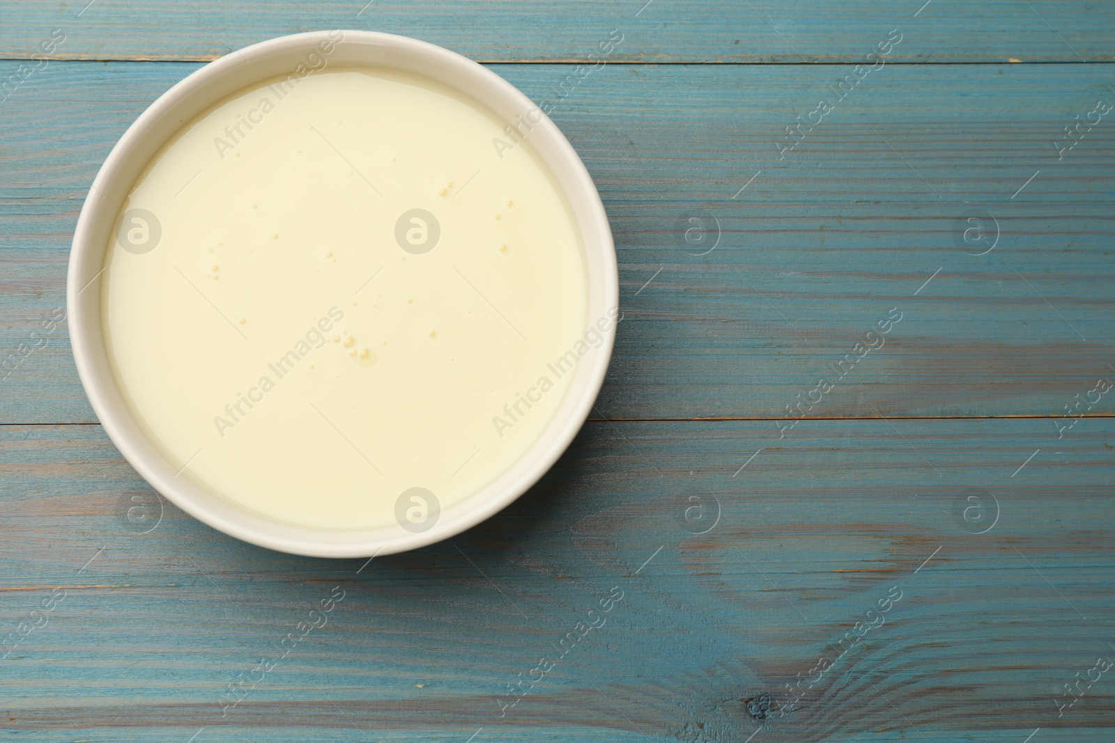 Photo of Condensed milk in bowl on light blue wooden table, top view. Space for text