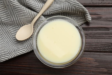 Photo of Condensed milk in bowl and spoon on wooden table, top view