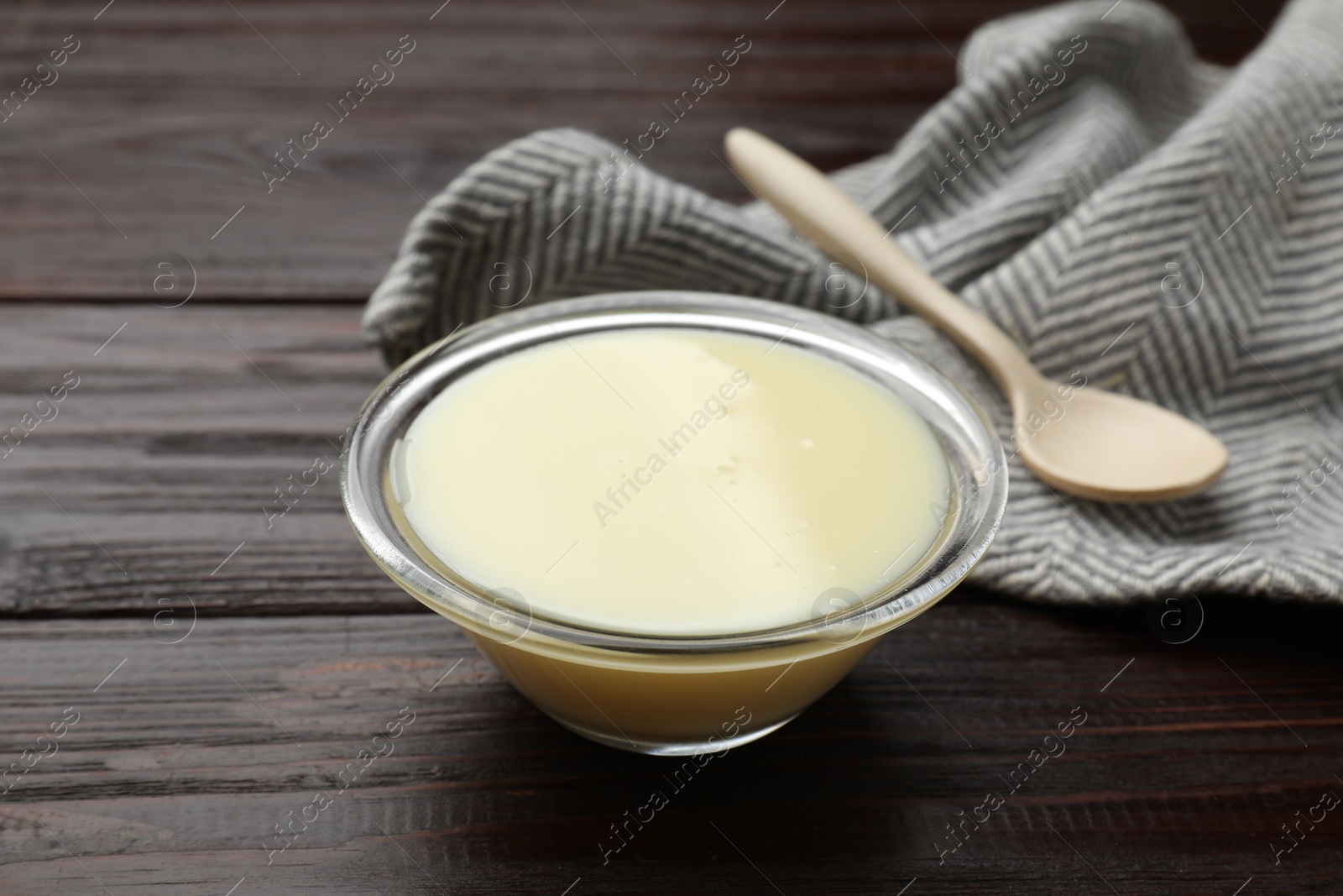 Photo of Condensed milk in bowl and spoon on wooden table, closeup