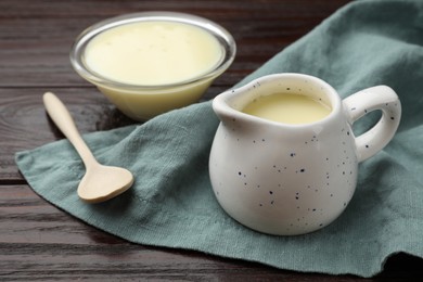 Photo of Condensed milk and spoon on wooden table, closeup