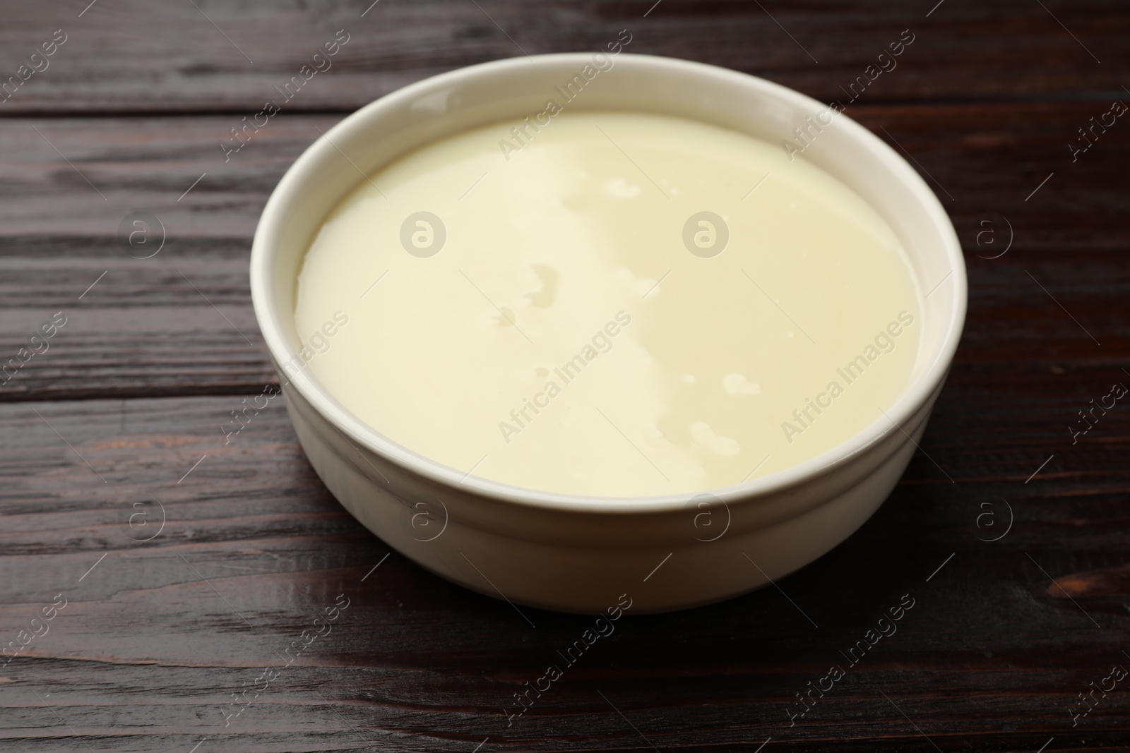 Photo of Condensed milk in bowl on wooden table, closeup