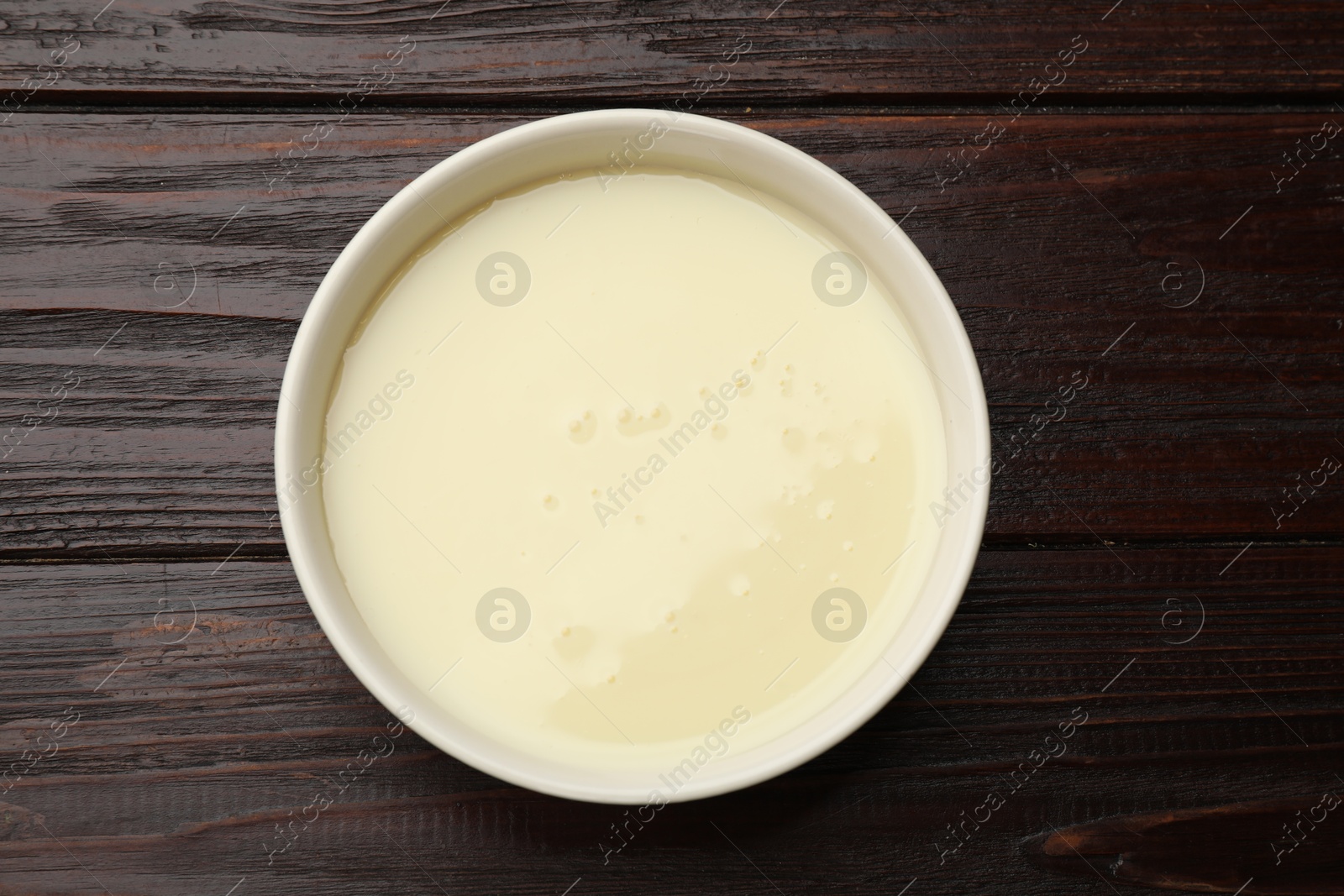 Photo of Condensed milk in bowl on wooden table, top view