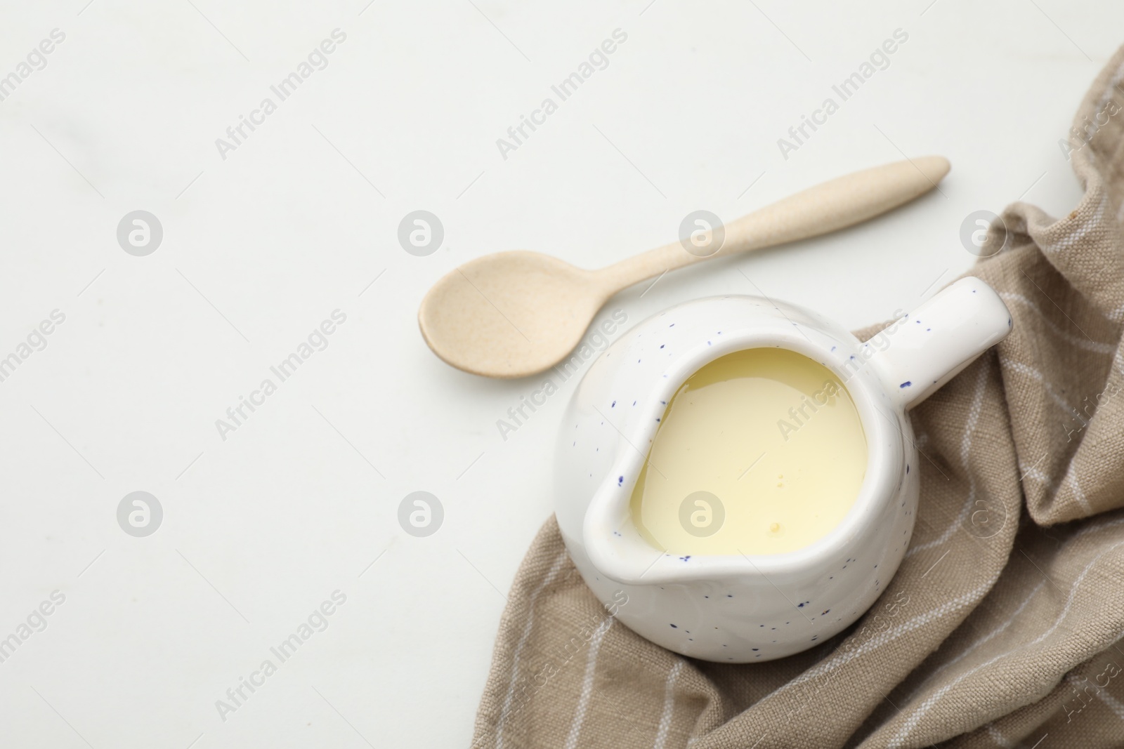 Photo of Condensed milk in jug and spoon on white marble table, top view. Space for text