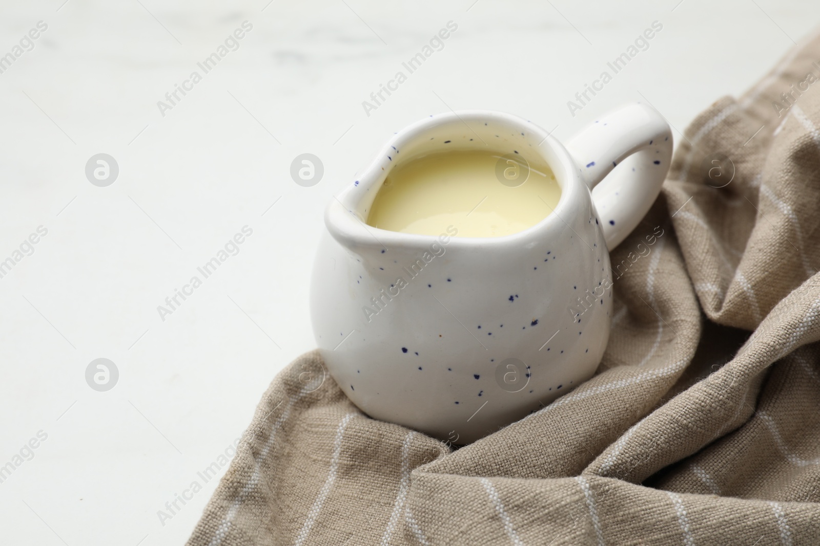 Photo of Condensed milk in jug on white marble table, closeup