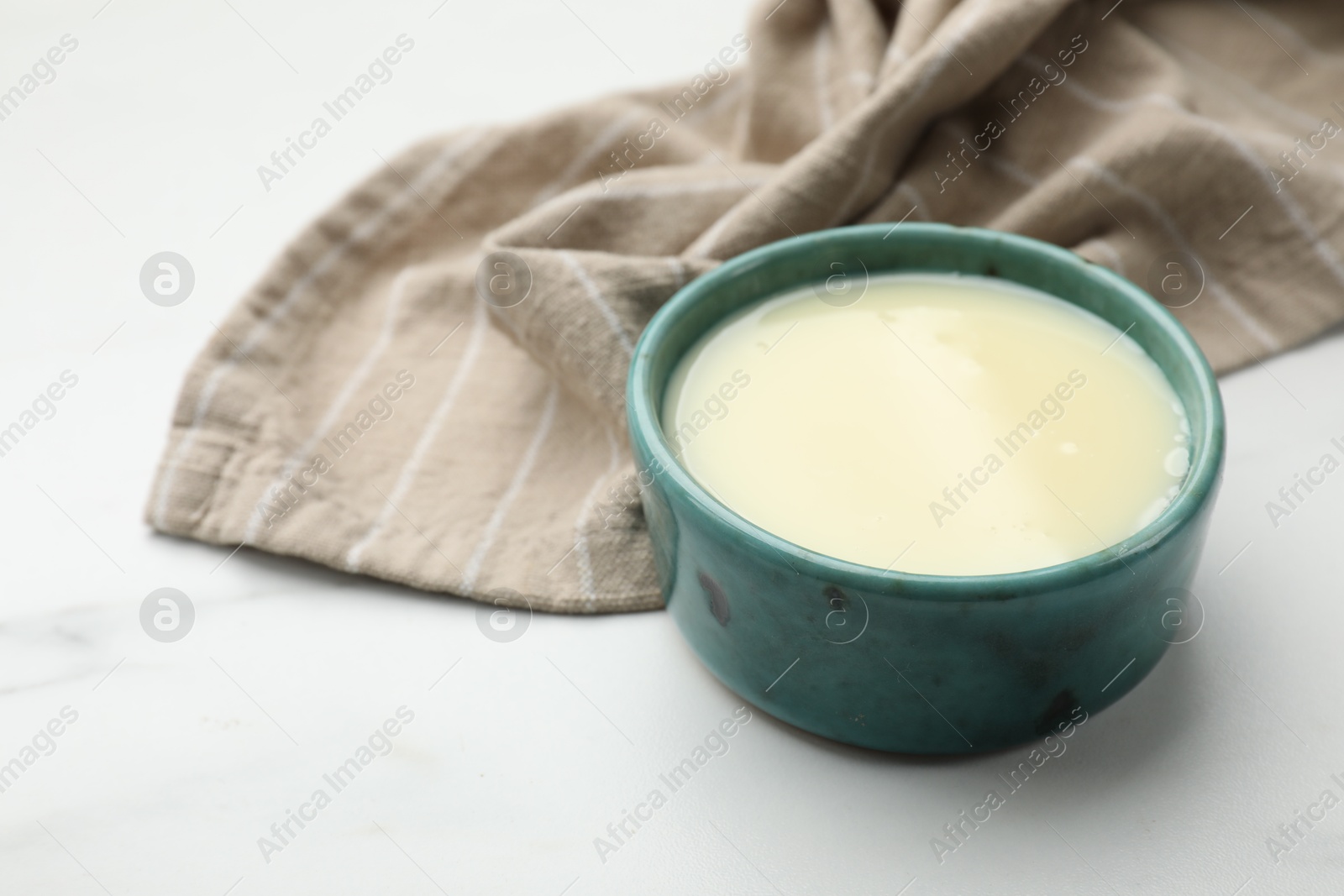 Photo of Condensed milk in bowl on white marble table, closeup. Space for text