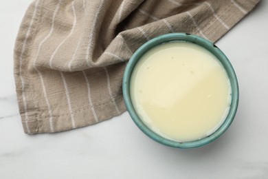 Photo of Condensed milk in bowl on white marble table, top view