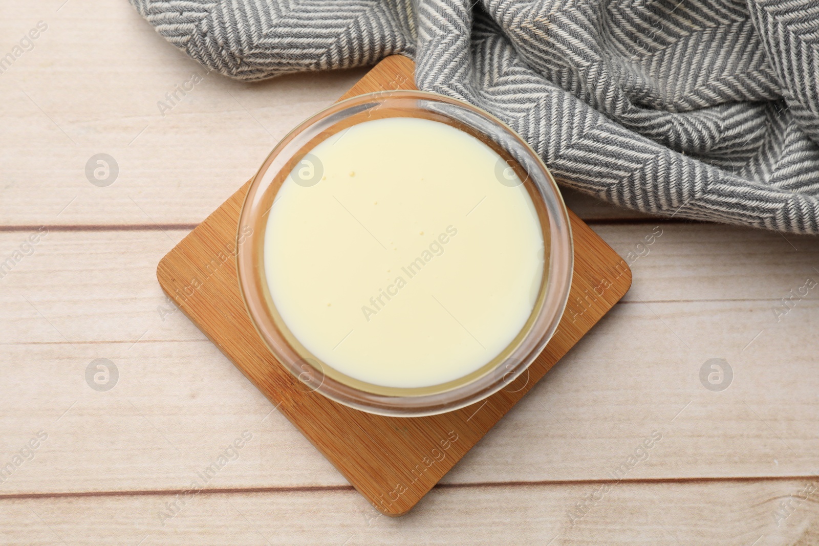 Photo of Condensed milk in bowl on light wooden table, top view