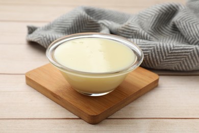 Photo of Condensed milk in bowl on light wooden table, closeup