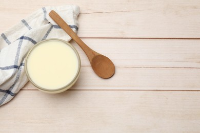 Photo of Condensed milk in bowl and spoon on light wooden table, top view. Space for text