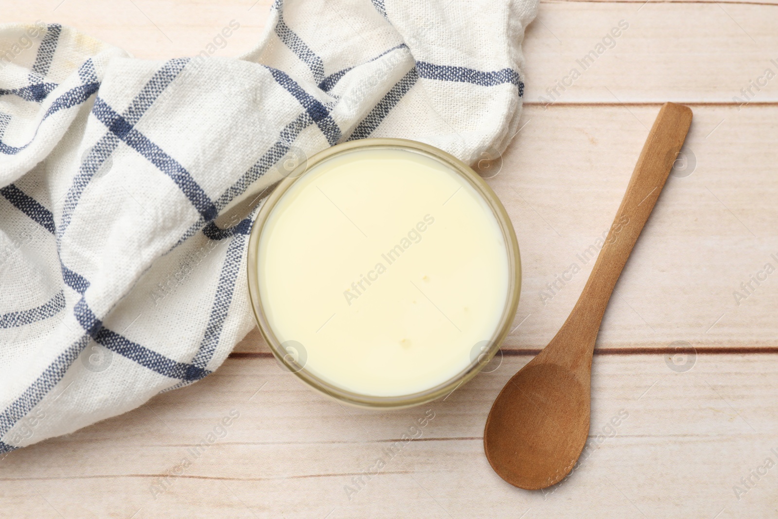 Photo of Condensed milk in bowl and spoon on light wooden table, top view