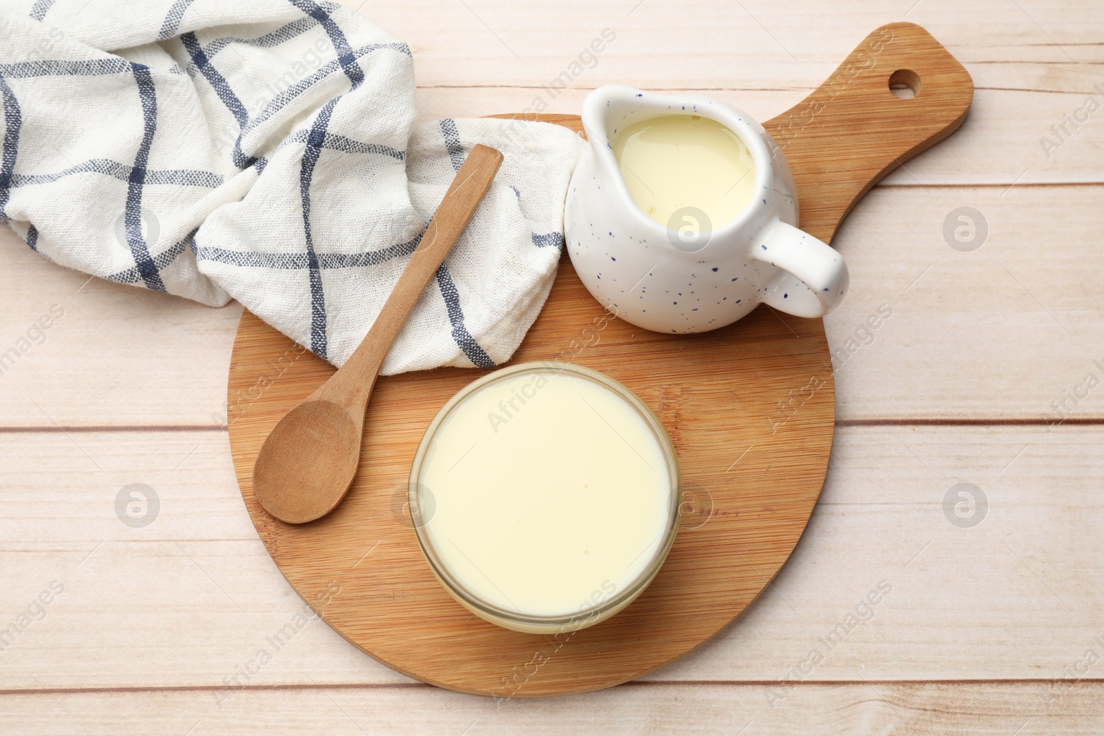 Photo of Condensed milk and spoon on light wooden table, top view