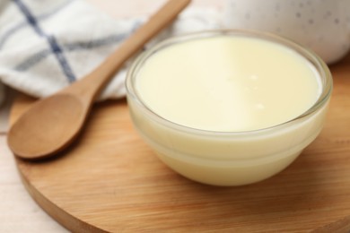 Photo of Condensed milk in bowl and spoon on light wooden table, closeup