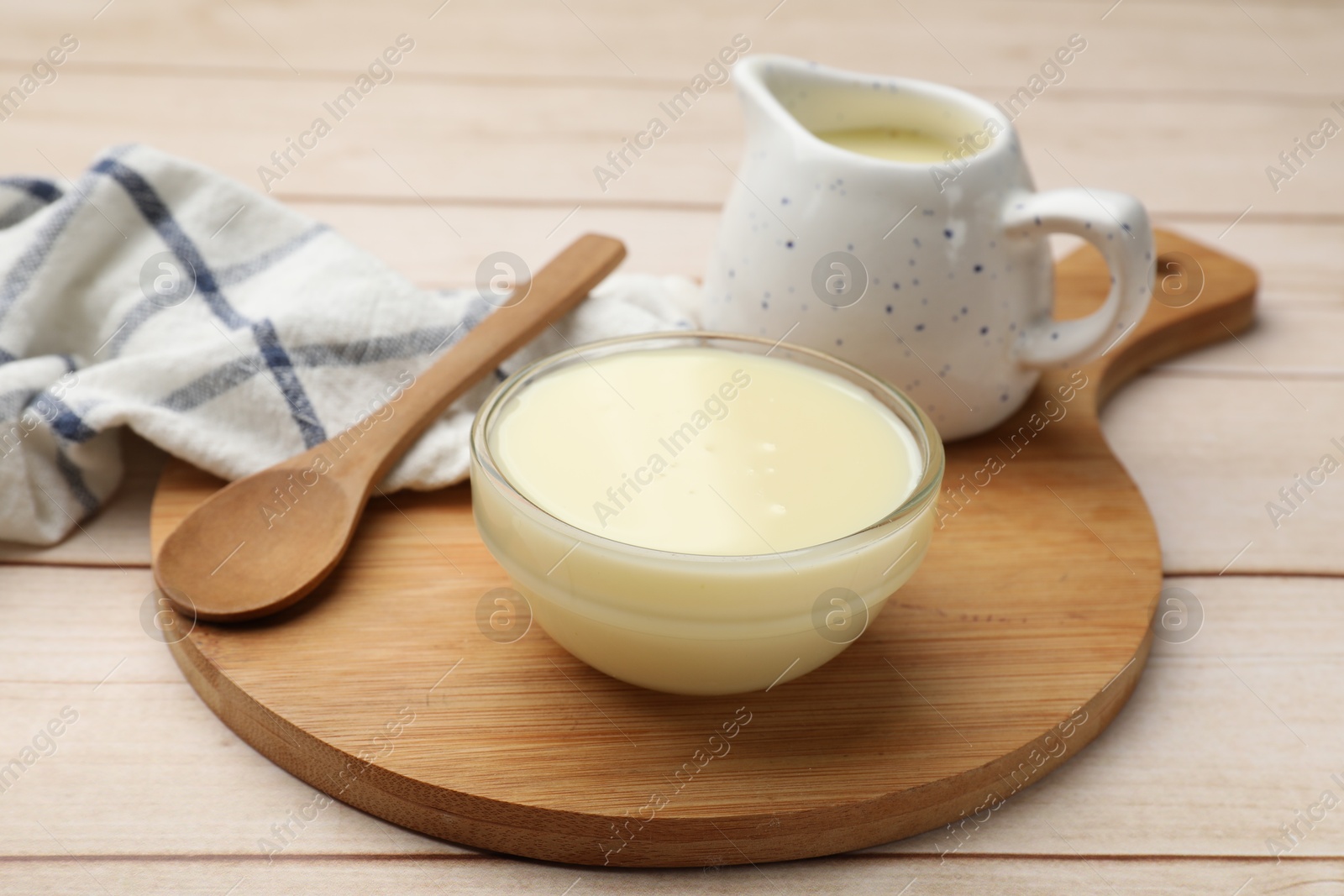 Photo of Condensed milk and spoon on light wooden table, closeup