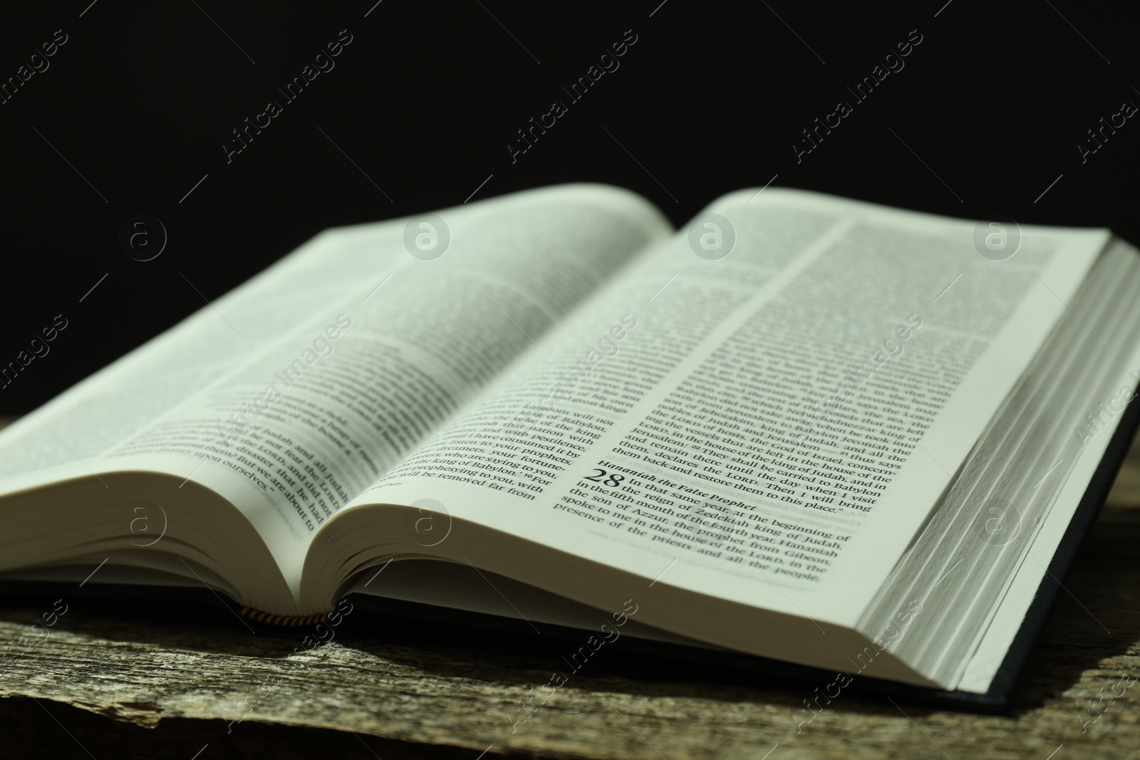 Photo of Open Holy Bible in English language on wooden table, closeup